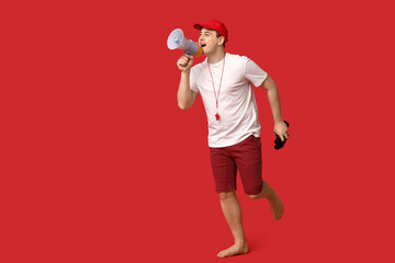 Wall Mural - Male lifeguard with megaphone and binoculars running on red background