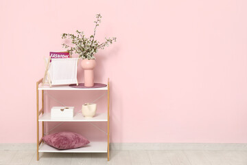 Wall Mural - Magazines in holder and vase with beautiful blooming branches on shelving unit near pink wall