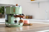 Modern coffee machine with cup of hot espresso and cupcake on table in kitchen