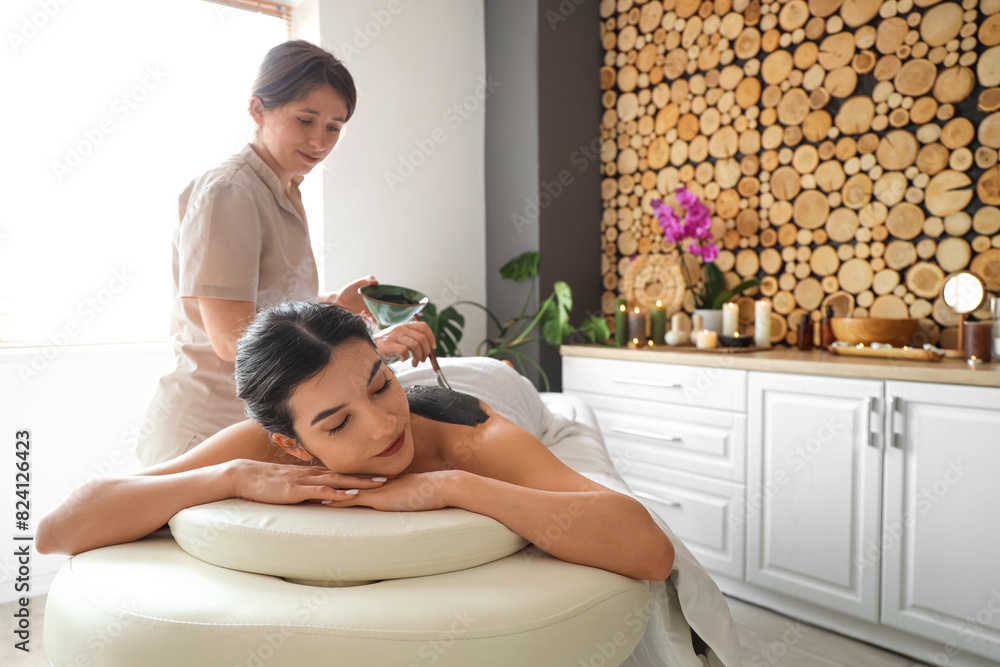 Young woman undergoing mud treatment on couch in spa salon