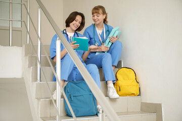 Canvas Print - Female medical interns with folders and copybooks sitting on stairs in clinic