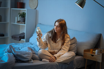 Wall Mural - Tired young woman with alarm clock suffering from insomnia in bedroom at night