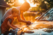 © VisualProduction - Caucasian father and son washing a car in their driveway during sunset.