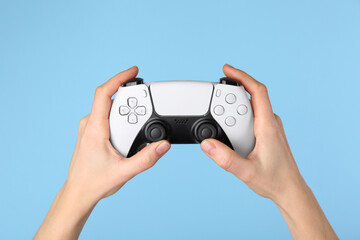 Wall Mural - Woman using game controller on light blue background, closeup