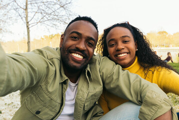 afro american couple taking a selfie sitting in a park