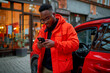 © MVProductions - Young african american man standing on the street and opening a car door while using a mobile phone