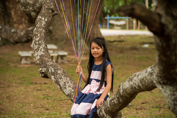 Wall Mural - Cheerful cute girl holding balloons running on green meadow sunrise golden vibrant sky happiness. Hands holding vibrant air balloons play on birthday party happy times summer on gold sky outdoor