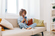 © SHOTPRIME STUDIO - Couch Comfort: A Happy Woman Holding a Smartphone, Relaxing and Gaming at Home'