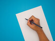© meeboonstudio - Right hand holding a pen for writing on empty white paper over a blue background.