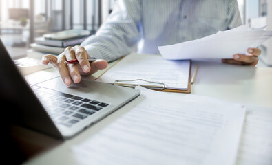 Wall Mural - Asian businessman using computer laptop working and reviewing document reports at office workplace. legal expert, professional lawyer reading and checking financial documents or insurance contract