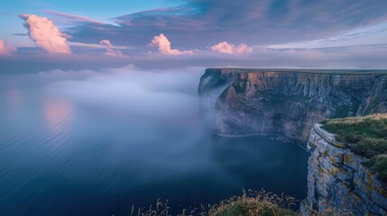 Wall Mural - Coastal cliffs overlooking a tranquil sea, where mist rises gently and the clouds above are softly lit by the early morning sun.