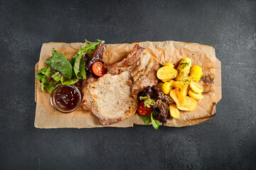 Sticker - Grilled bone-in pork chop accompanied by seasoned roasted potatoes and a side of salad, top view. A hearty and satisfying traditional meal