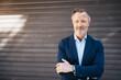 © contrastwerkstatt - Confident mature businessman wearing a suit, standing with arms crossed in front of a metal shutter door. Professional and composed.