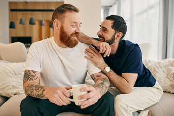 A gay couple in casual attire relax on a couch, enjoying each others company and sipping coffee in a modern living room setting.