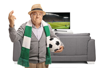 Canvas Print - Elderly fan with a football and a scarf holding his fingers crossed for luck for the football match on tv