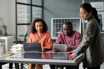 Aufkleber - Young Asian businesswoman touching solar panel model while her colleagues preparing new projects at working meeting