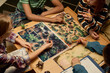 © pressmaster - High angle of four intercultural youngsters gathered by table with new board game and playing while one of girls throwing dice