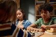 © pressmaster - Serious African American schoolboy in striped t-shirt thinking of next move and looking at chess board with pawns and other figurines
