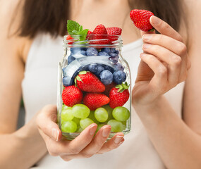 Wall Mural - female hands holding a glass jar with strawberries, blueberries and grapes close-up