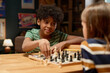 © pressmaster - Youthful African American schoolboy looking at checkmate and moving pawn or other chess figurine on board while sitting by table