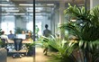 © OLGA - Modern office with glass walls, lush green plants, and busy staff.