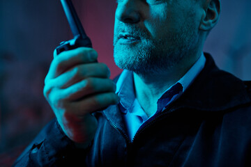 Cropped shot of mature male guard speaking to colleague in walkie-talkie while notifying situation during night duty watch