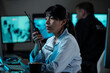 © pressmaster - Young serious Hispanic female officer of surveillance room reporting situation on walkie-talkie while looking at computer screen