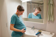 © Johnér - Pregnant young woman touching abdomen by hair trimmer in front of mirror at bathroom
