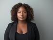 © James - African American woman, plus size model in black business attire with curly hair, professional, gray background.
