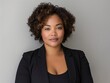 © James - African American woman, plus size model in black business attire with curly hair, professional, gray background.