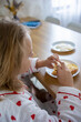 © evgeniia_1010 - A cute blonde girl in beautiful pajamas is sitting at a cozy table in the kitchen and enjoying a delicious and healthy breakfast. The concept of proper and balanced nutrition.