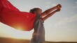 © maxximmm - girl with the cloak. concept of a happy childhood and family for a child. little girl in a superhero costume stretched hand forward, a lifestyle red cape and a blue T-shirt, sunset on the background