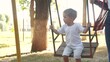 © maxximmm - little boy swings on a swing. concept of a happy childhood and loving family. a child in white clothes swings on a swing on the playground, the boy is being lifestyle filmed by his parents