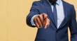 © Carmen - Close up of African-American business man in blue suit, pointing finger at camera, against pale yellow background with copy space