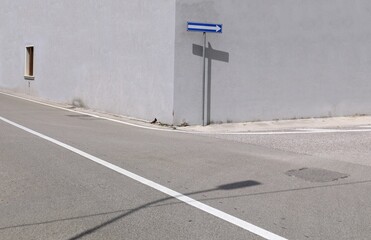 Directional arrow traffic sign on a pole at corner street with gray plaster wall on behind. Urban street in front. Background for copy space.