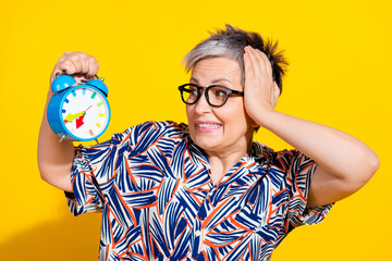 Sticker - Photo portrait of nice pensioner female look worried alarm clock wear trendy colorful outfit isolated on yellow color background