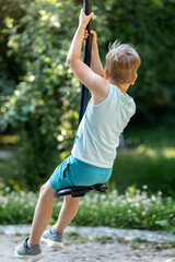 Wall Mural - A boy in light blue clothes on a swing from behind, on a sunny bokeh nature background