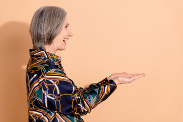 Poster - Side profile photo of overjoyed ecstatic woman wear print blouse look empty space palms hold product isolated on beige color background