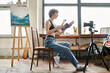 © LIGHTFIELD STUDIOS - Pretty woman sitting in chair, showing how to paint on camera.