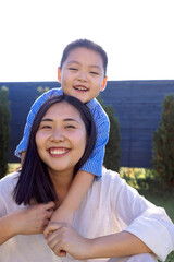 Asian laughing mom and son are hugging on a green lawn