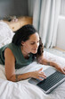 © Nicola Suttle/Stocksy - Woman browsing netbook on bed at home
