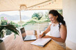 © Nicola Suttle/Stocksy - Cheerful woman writing notes during online work on sunny day