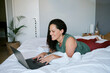 © Nicola Suttle/Stocksy - Smiling woman using laptop on bed