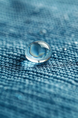 Wall Mural - A small, clear, round droplet of water sits on a blue fabric