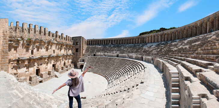 Happy woman in hat open arms in free happiness standing and posing -  Roman amphitheater of Aspendos, Belkiz - Antalya, Turkey