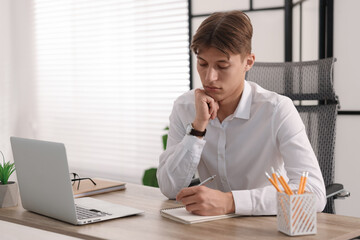 Wall Mural - Man taking notes during webinar at wooden table indoors