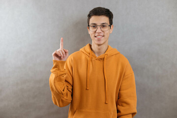 Portrait of a smiling teenage boy on a grey background pointing up. Copy space, close up.