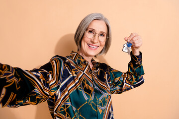 Poster - Photo of satisfied senior person with grey hair wear blouse in glasses demonstrate keys making selfie isolated on beige color background