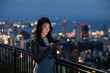 © Heng Yu/Stocksy - Woman Using Smartphone Overlooking City Lights