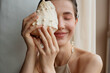 © Amor Burakova/Stocksy - Happy woman closes her eye with a seashell